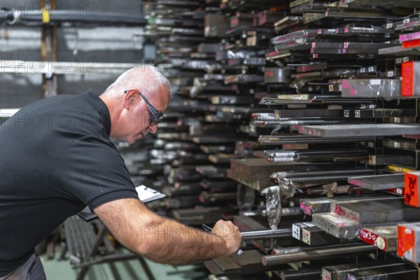 Mature caucasian male inspector doing inventory and measuring metal bars in a factory
