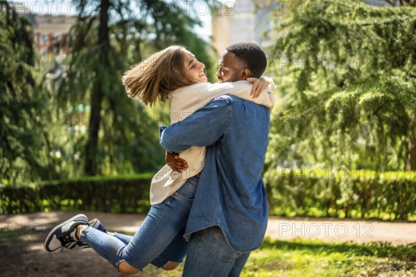 Caucasian woman jumping to hug her african male partner in a park