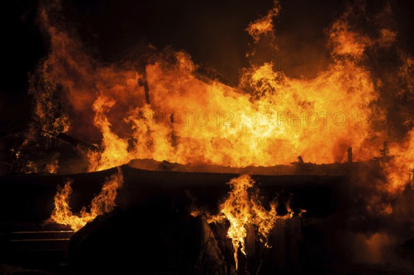 Arson or nature disaster, burning fire flame on wooden house roof