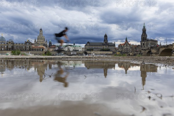 The Dresden silhouette with a cyclist and dark clouds behind the Church of Our Lady is reflected in