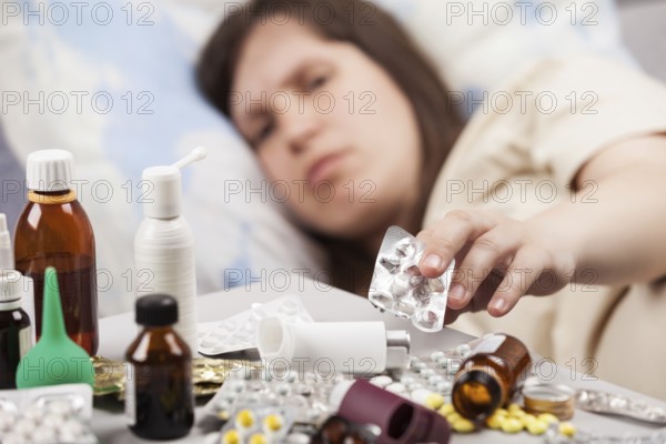 Adult woman patient hand holding vitamin pills lying down bed for cold and flu illness relief