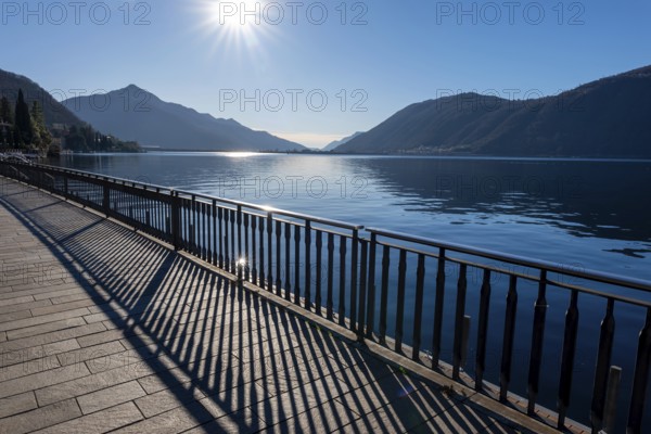 Shadow of a Railing on the Street on the Waterfront to Lake Ceresio with Mountain and Sunbeam in