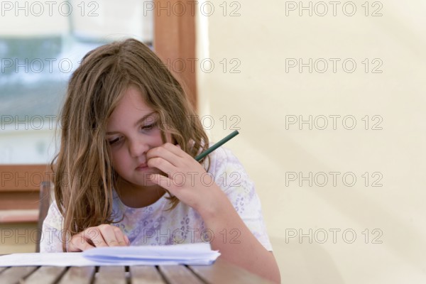 Close-up of a beautiful blonde girl in a colorful dress concentrating on school homework