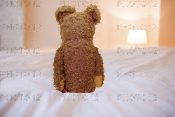 Teddy bear sitting on a bed, symbolic image Lonely childhood