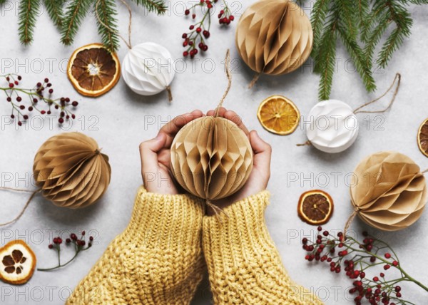 Hands holding a beige paper ball surrounded by Christmas decorations on a table. Handmade honeycomb