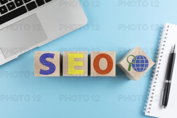 top view of letters SEO and internet search symbol on wooden cubes on blue background with laptop
