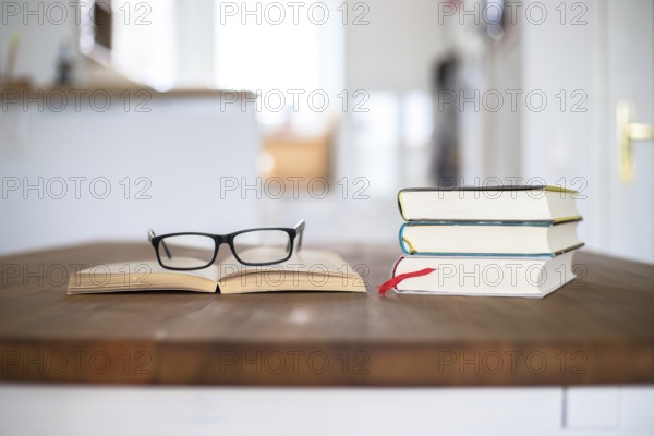 Stack of books and glasses lying on wooden desk at home. Knowledge and science