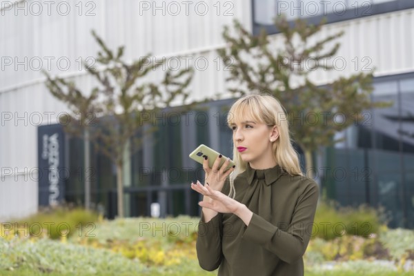 Caucasian blonde entrepreneur girl in a business park sending an audio note with the phone