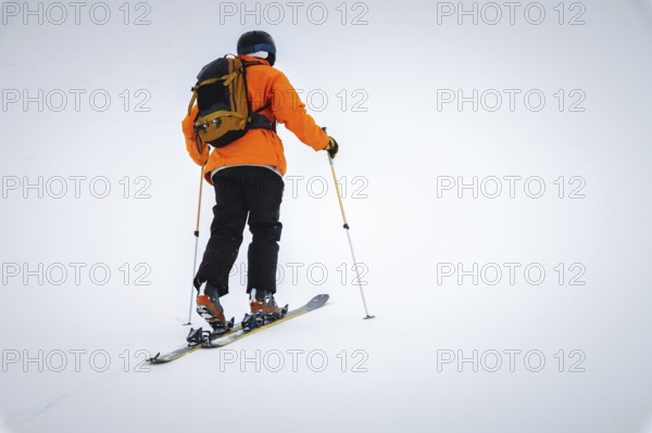 A skier climbs a snow-covered ridge in the fog with a backpack, ski tour. Extreme sport in the