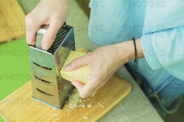 Close-up of a woman's hands rub a parmesan cheese on a metal grater on a green table