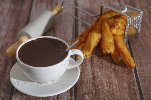 White cup of hot chocolate with churros typical spanish breakfast on a wooden table