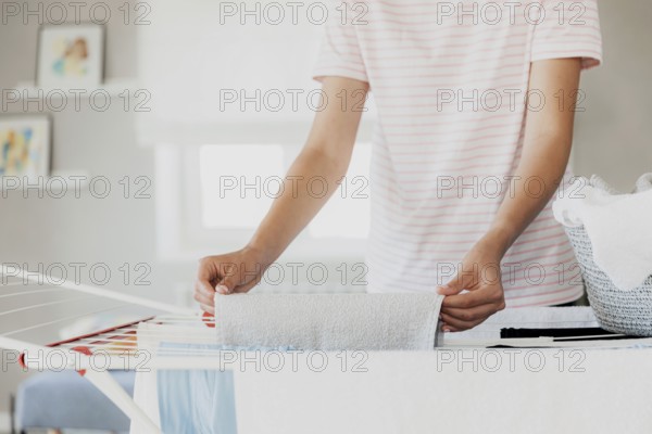 Woman hanging clean wet clothes laundry on drying rack at home in room. Detail of female housewife