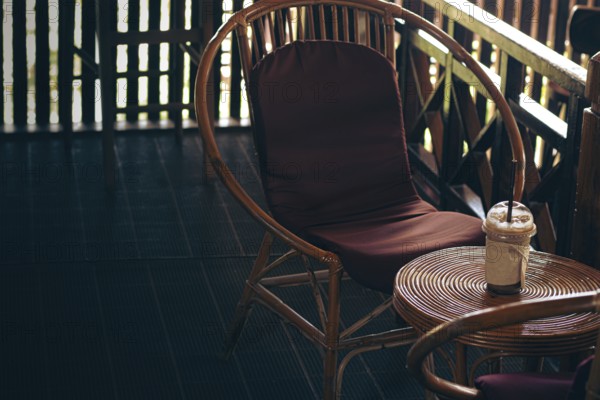 Rattan chair with a brown cushion beside a small circle table holding an iced coffee on a cozy