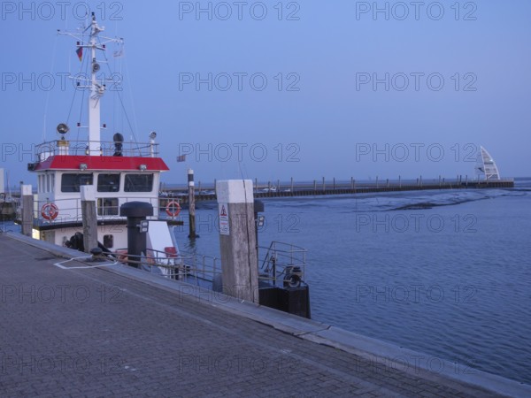 A ship lies at the dock of a harbour at dusk, the calm waters reflect the evening light, juist,