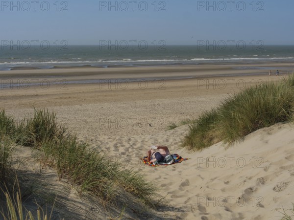 Person relaxing on a blanket in a sand dune on the beach, overlooking the calm sea, de haan,