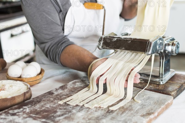 Baker cutting raw dough into tagliatelle pasta machine wooden board