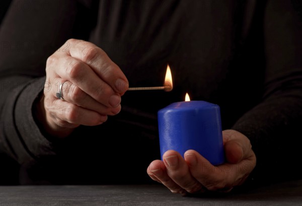 Hands of a woman lighting a blue candle with a match