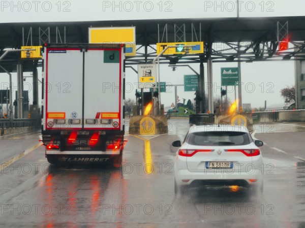Car waiting at a toll booth with traffic lights and payment lanes on a rainy day, A1 A8 highway