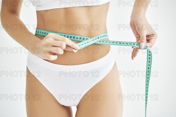 Young slim woman measuring her waist by measure tape on white background. Healthy lifestyle, diet