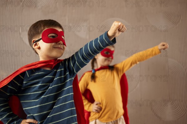 Portrait of a team of two young superheroes, brother and sister, over beige background. Superhero