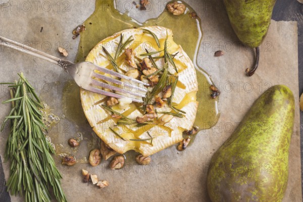 Delicious beautiful baked camembert with fork. Cheese with honey, walnuts, herbs and pears
