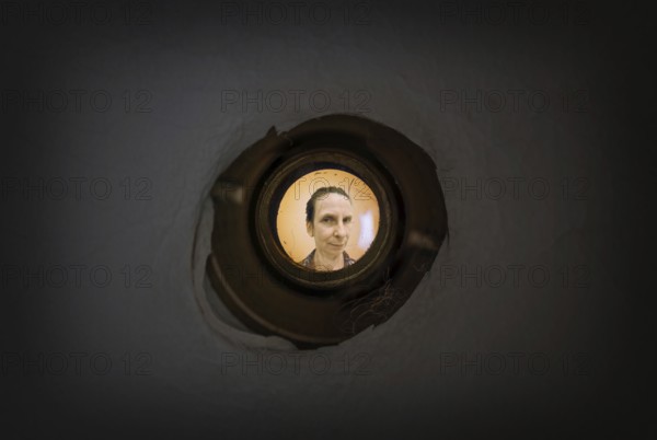 Woman seen out of focus through the old dirty peephole of the front door of a dark apartment