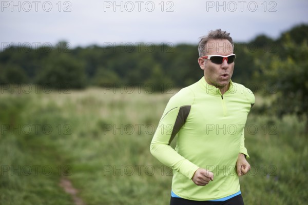 Healthy fit man wearing sunglasses jogging through rural grassland on a country track with copy