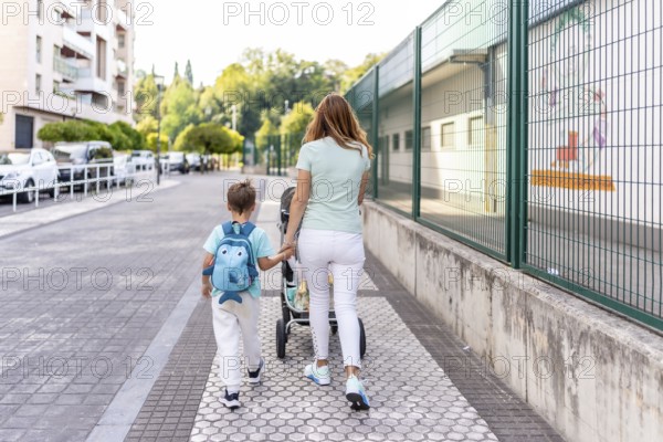 Rear view of a mother and son going to school together holding hands on the first day of school
