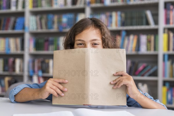 Boy covering his face with book library