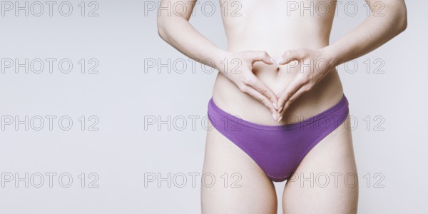 hands make heart shape over belly as women's health self care or pregnancy concept
