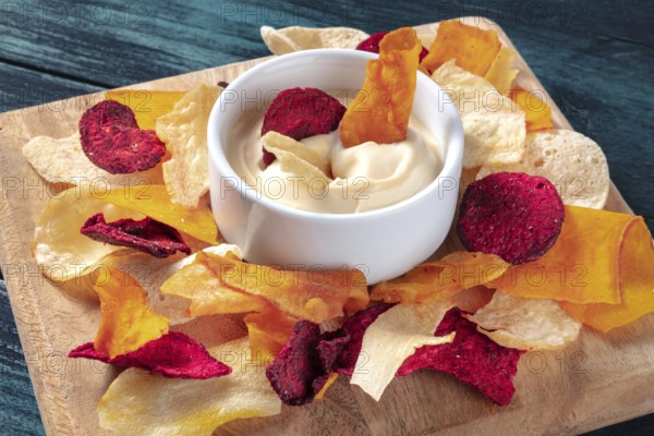 Vegetable chips with a dip on a wooden board, a healthy vegan snack