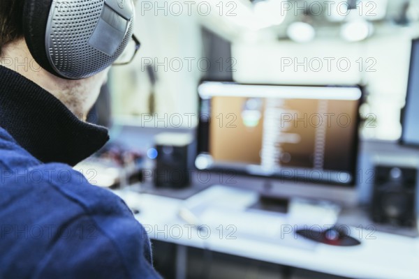 Young man with headphones is sitting in the recording studio, buttons, studio, screens and