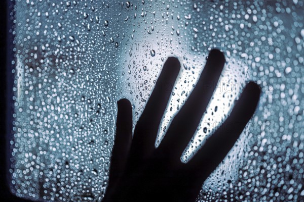 Close up of hand silhouette on window with water drops, night