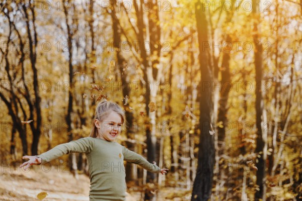 Small happy smiling little caucasian child girl playing with yellow leaves in autumn forest or