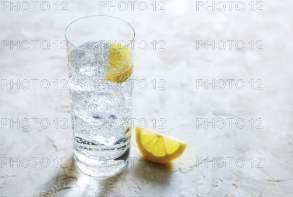 Fresh carbonated mineral water with ice cubes and lemon slices in a drinking glass, refreshing