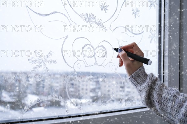 Female hand painting Christmas deer painted on window glass. Christmas winter decor on the window