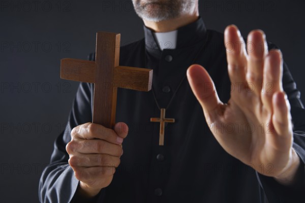 Priest holding cross of wood praying in foreground