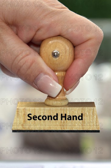 A woman's hand holds a wooden stamp with the inscription: Second Hand