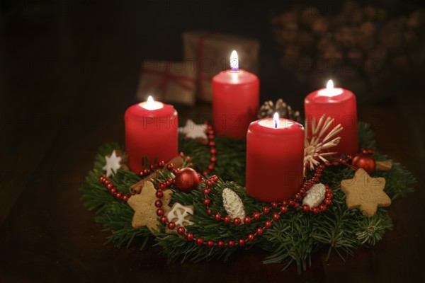 Advent wreath from fir branches with red lit candles and Christmas decoration, some gifts blurred