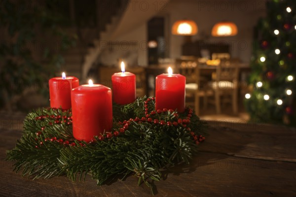 Decorated Advent wreath from fir branches with red burning candles on a dark wooden table, living