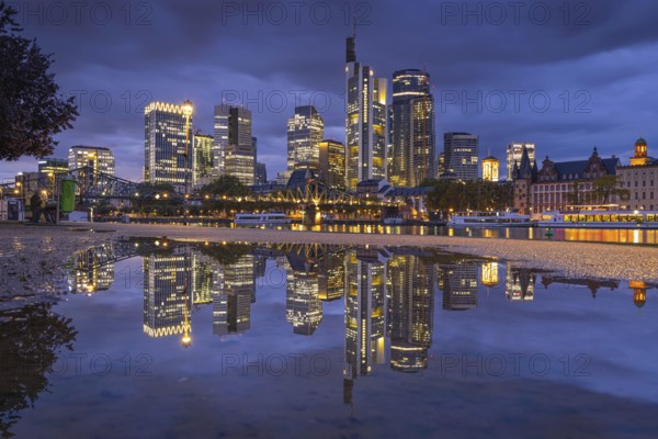 Clouds pass over the glowing Frankfurt bank skyline reflected in a puddle in the evening, Mainufer,
