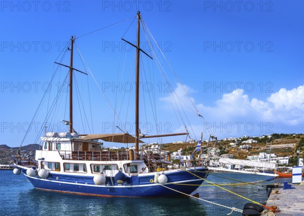 Schooner moored at jetty of typical Greek island. Beautiful whitewashed houses on hills and by