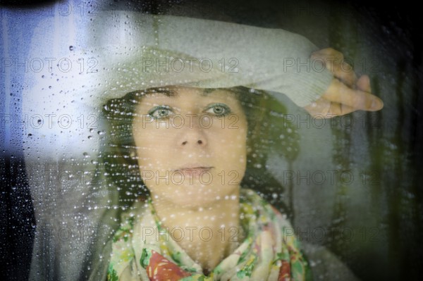 Young woman looks through the window in rainy weather