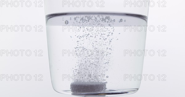 Tablets Falling and Dissolving into a Glass of Water against White Background