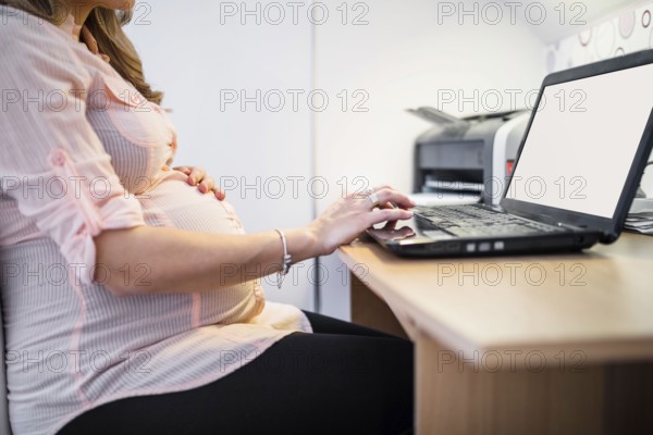 Midsection view pregnant woman using laptop wooden desk