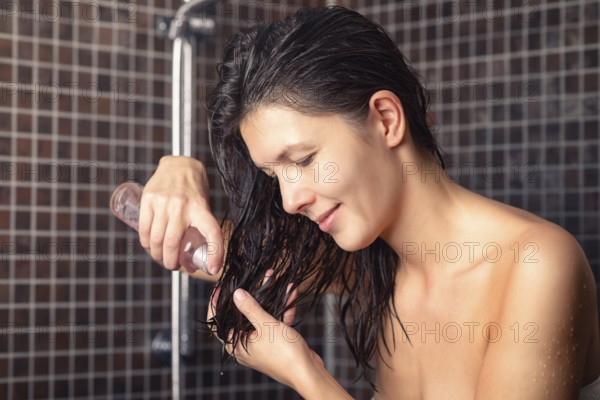 Young woman about to apply hair oil to her newly washed hair standing in the bathroom in a towel