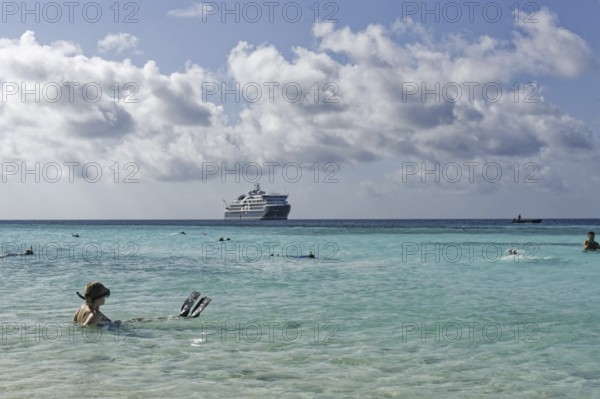 Snorkeller sitting in turquoise blue water, cruise ship SH DIana in the background, blue, slightly
