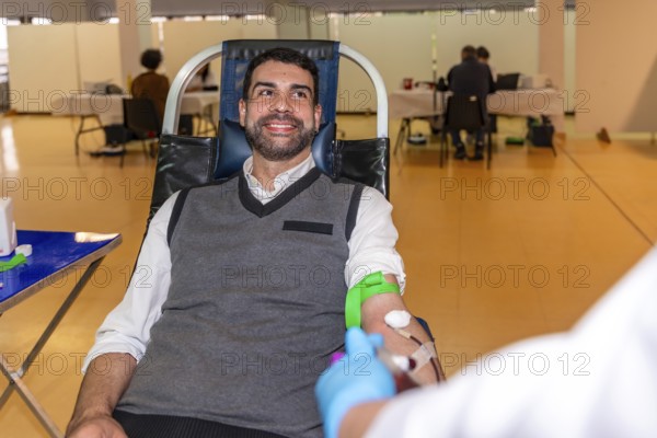 Altruist smiling man sitting on comfortable chair while donating blood in a pavilion