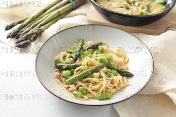 Spaghetti carbonara variation with green asparagus served in a plate, ingredients and napkin on a