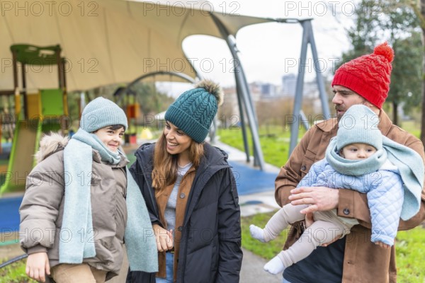 Smiling parents holding their children, a toddler and a baby, wearing warm winter clothes while